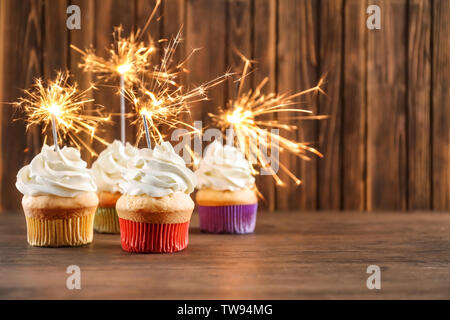 Birthday cupcakes with sparklers on table against wooden background Stock Photo