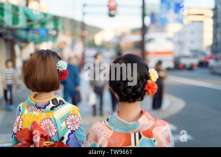 Two Japanese girls in bright Yukatas, and colorful flowers in their hair, walking on the streets of Kyoto, Japan. Stock Photo