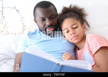 African American man reading bedtime story to his daughter in bed Stock Photo