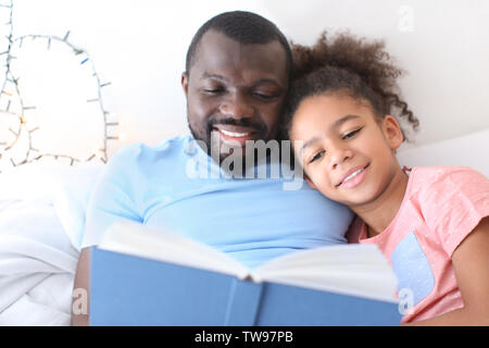 African American man reading bedtime story to his daughter in bed Stock Photo