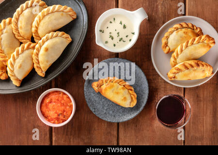 Empanadas with sauces and wine, shot from the top on a dark rustic wooden background Stock Photo