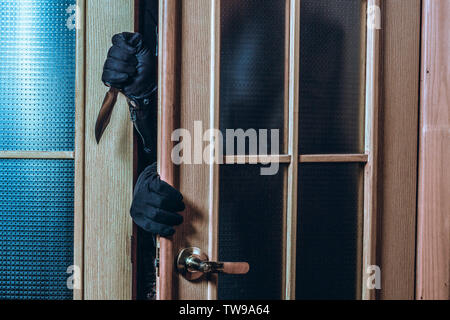 The criminal enters the house in the dark. Man's hands in black gloves and a knife Stock Photo