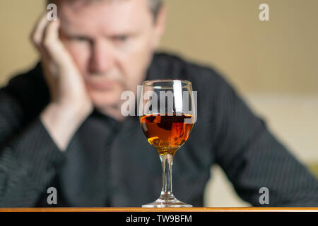 Tired man leaning his head on a glass of brandy. Man out of focus Stock Photo