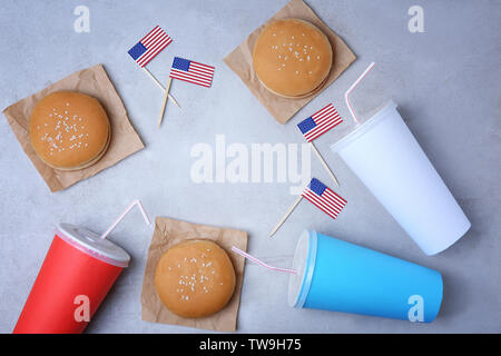 Tasty hamburgers, cups with drinks and American flags on light background Stock Photo