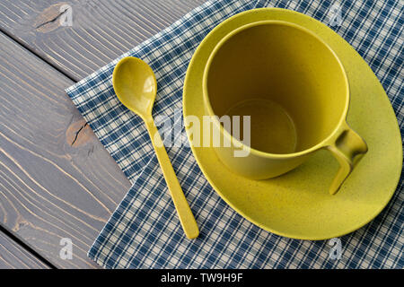 Yellow cup on a saucer with a spoon. Utensils of bamboo, with a checkered napkin on a wooden table. Shallow depth of field. Stock Photo