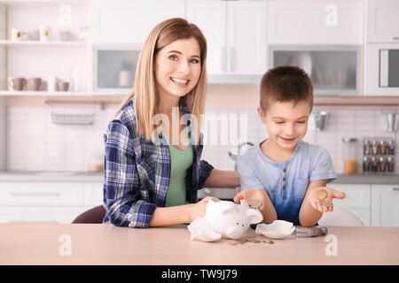 Mother and little son with broken piggy bank on table at home Stock Photo