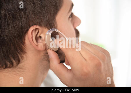 Young man putting hearing aid in ear indoors Stock Photo