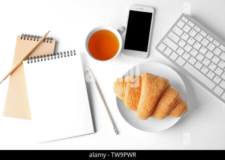 Tasty croissant, cup of tea, smartphone and notebooks on white background Stock Photo