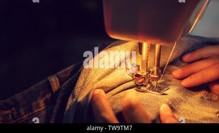 close up of a woman sewing blue denim jeans with a sewing machine Stock Photo