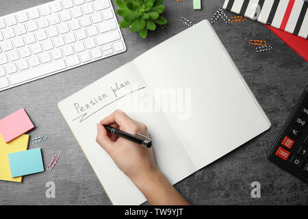 Woman writing text 'Pension plan' in notebook Stock Photo