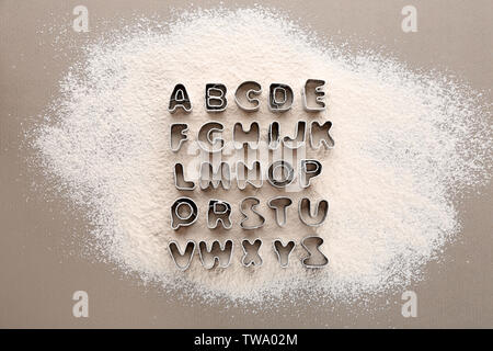 Cookie cutters in shape of alphabet letters on scattered flour Stock Photo