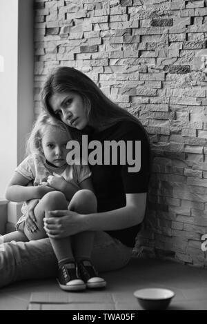 Homeless poor woman with little daughter sitting near brick wall Stock Photo