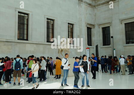 Group of Asian visitors stand around the marble Roman statue of a youth on horseback in the Queen Elizabeth II Great Court inside the British Museum. Stock Photo