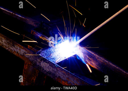 Welder worker performs jump welding. Man welder in protective gloves performs arc-welding process of metal structures. Flying sparks from the welding Stock Photo