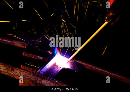 Welder worker performs jump welding. Man welder in protective gloves performs arc-welding process of metal structures. Flying sparks from the welding Stock Photo