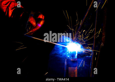 Welder worker performs jump welding. Man welder in protective gloves performs arc-welding process of metal structures. Flying sparks from the welding Stock Photo