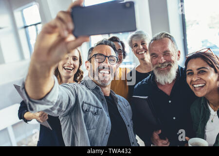 Successful business team taking selfie together. Multiracial group of people taking selfie at office. Stock Photo
