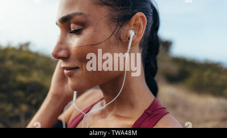 Pretty young woman wearing earphones to listen music before starting her running workout. Fit female athlete before her run outdoors. Stock Photo