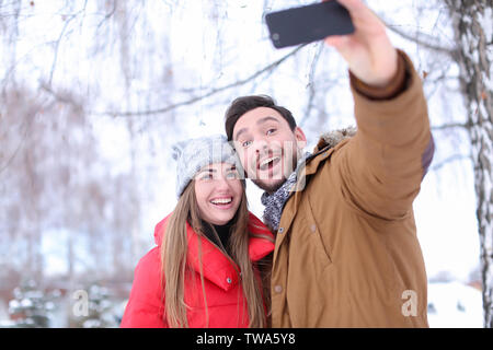 Young couple taking selfie in snowy park on winter vacation Stock Photo