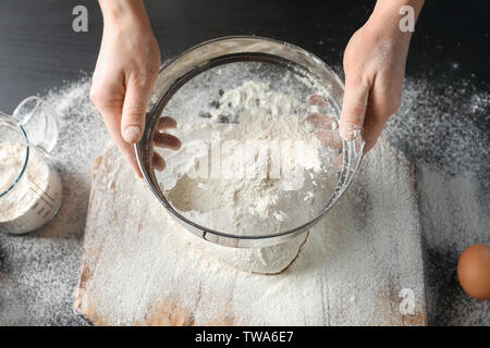 Woman sifting flour over dough on table Stock Photo