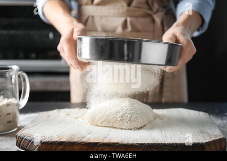Woman sifting flour over dough on table Stock Photo
