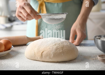 Woman sifting flour over dough on table Stock Photo