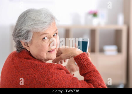 Mature woman with hearing aid using smartphone indoors Stock Photo