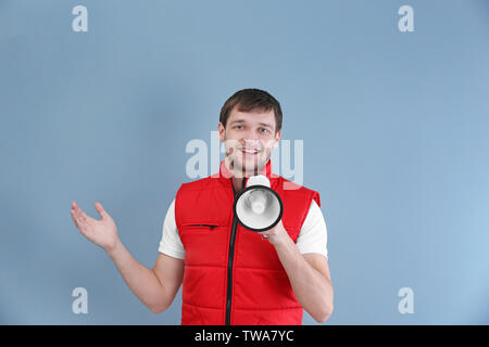 Handsome man in red vest with megaphone on color background Stock Photo