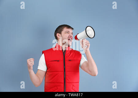 Handsome man in red vest shouting into megaphone on color background Stock Photo