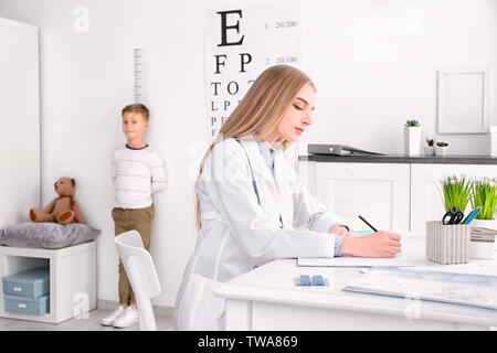 Young female doctor writing down results after measurement of little boy's height in hospital Stock Photo