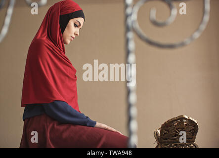 Young Muslim woman reading Koran, indoors Stock Photo