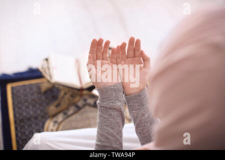 Young Muslim woman praying, indoors. Focus on hands Stock Photo