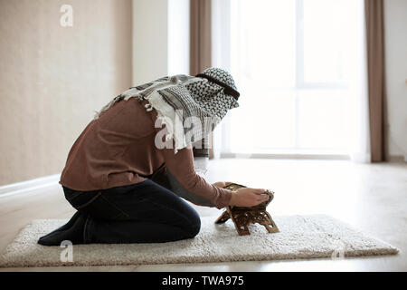 Young Muslim man reading Koran, indoors Stock Photo