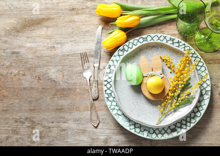 Beautiful festive Easter table setting with painted eggs and mimosa on wooden background Stock Photo