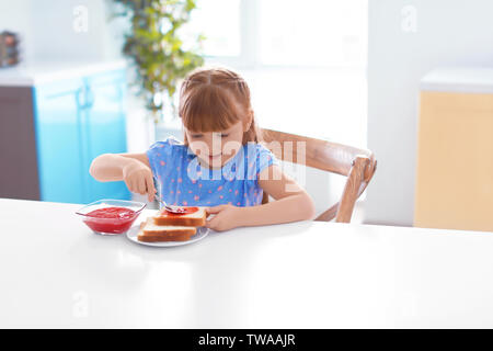 Cute little girl spreading jam on toast at home Stock Photo