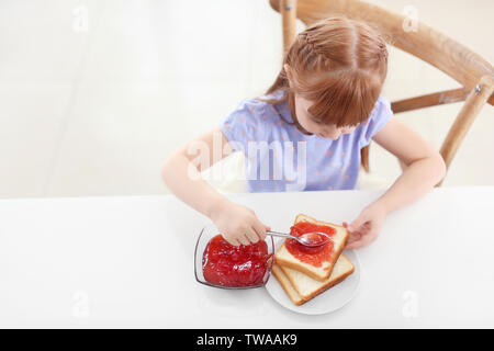 Cute little girl spreading jam on toast at home Stock Photo