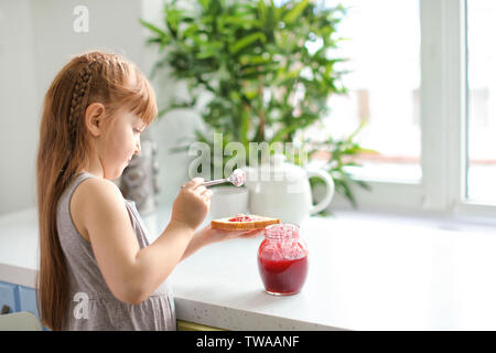 Cute little girl spreading jam on toast at home Stock Photo