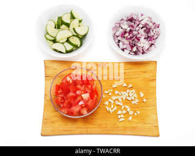 Sliced tomato in a transparent bowl and chopped garlic on a cutting board. White background. Sliced red onions and cucumbers in a white bowls Stock Photo