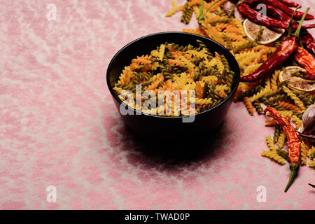 delicious colorful Italian pasta in ceramic plate with spoon , chili pepper, orange, garlic, star anise on pink textured background, copy space Stock Photo