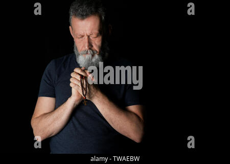Religious senior man praying on black background Stock Photo