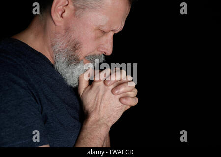 Religious senior man praying on black background Stock Photo
