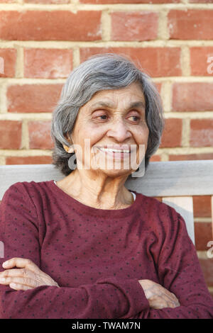 Old elderly Asian Indian woman sitting with a smiling face, depicting health and happiness in old age and retirement Stock Photo