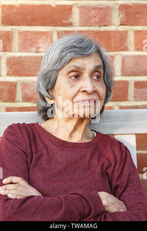 Elderly Asian Indian woman sitting alone. Healthy and slim appearance, may also depict loneliness or depression in old age. Stock Photo
