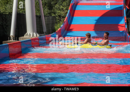 Happy family after riding down the water park structure in yellow inflatable double ring. Father and son, adult and teenager boy are enjoying weekend Stock Photo