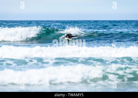Surfer man with surfboard is paddling on the wave. Guy in surfing wet suit is paddling the waves of cold atlantic ocean in Galicia, Spain. Stock Photo
