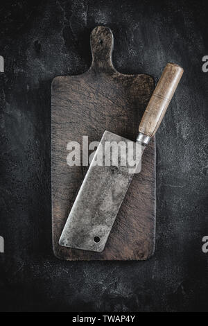 Old Butcher Meat Cleaver and Rustic Brown Wood Chopping Board on Dark Background Stock Photo