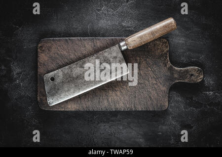 Old Butcher Meat Cleaver and Rustic Brown Wood Chopping Board on Dark Background Stock Photo