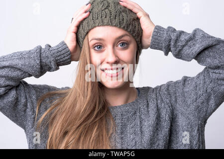 Portrait of young beautiful woman wearing knitted cap with white toothy healthy smile on light gray background. Stock Photo