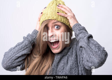Close up portrait of expressive young woman screaming with hands on head on light gray background. Stock Photo