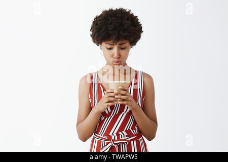 Studio shot of upset and gloomy silly girlfriend with afro hairstyle and dark skin pursing lips and gazing with sadness at empty paper cup of coffee Stock Photo